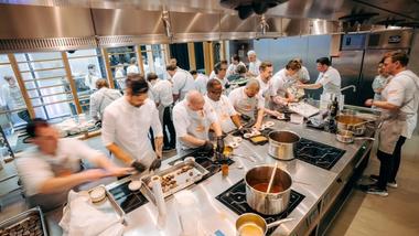 A team of Unilever Food Solutions chefs in a busy kitchen prepare food. Various pans can be seen on stovetops.
