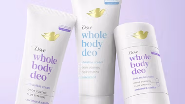 Three Dove ‘Whole Body Deo’ deodorant products displayed against a soft purple background. The products include two tubes labelled ‘invisible cream’ for odour control with vitamins – one coconut and vanilla scented and one unscented – and a white anti friction stick also in the coconut and vanilla scent. Each item features the Dove gold bird logo and clean, minimalist packaging.